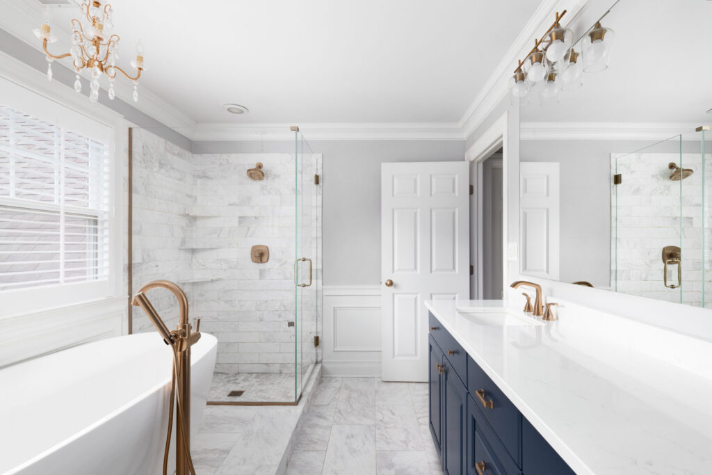 Luxury bathroom remodel with blue vanity, marble shower walls, and freestanding tub