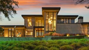 Modern luxury home exterior with large glass windows lit at dusk