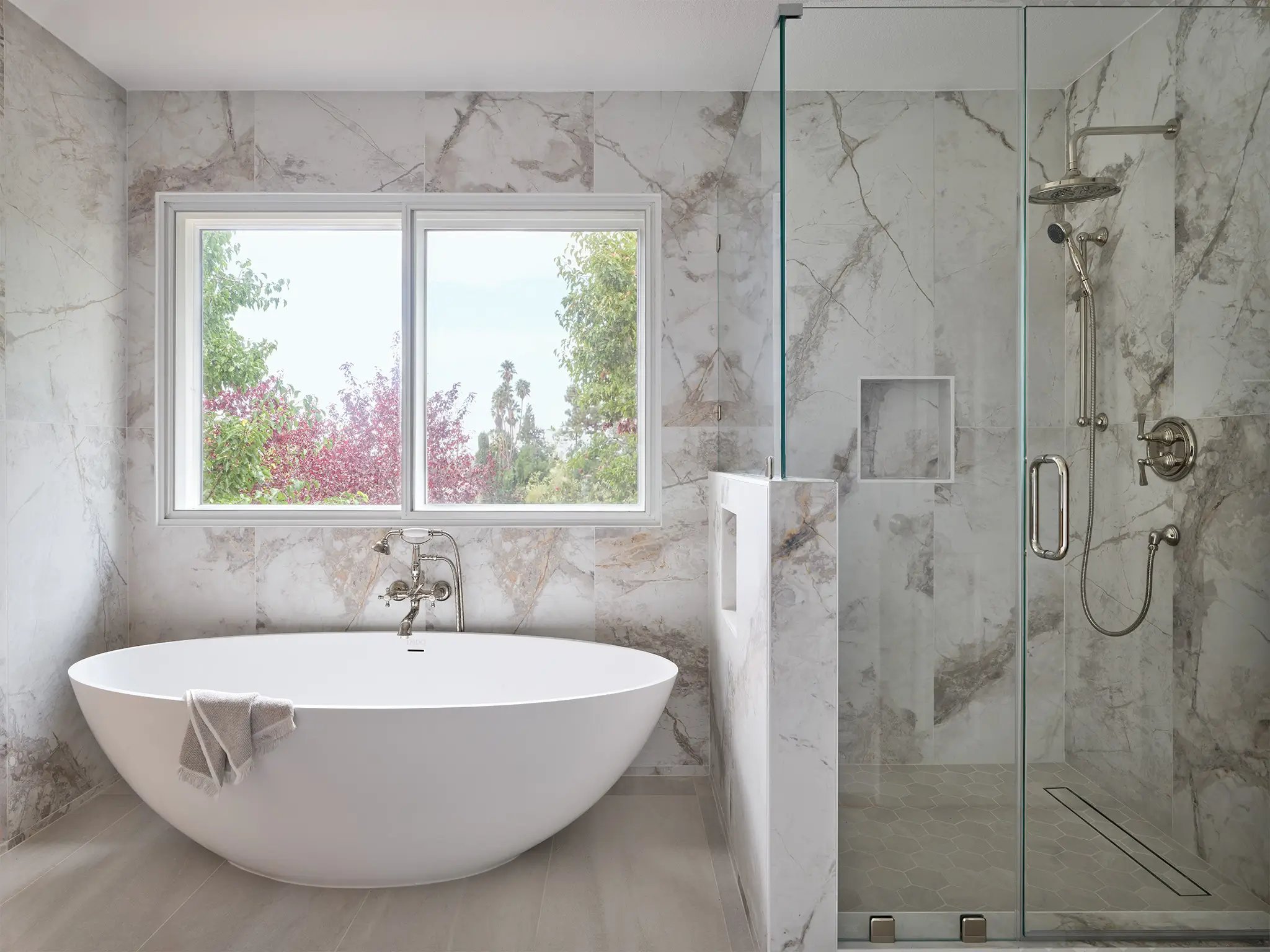 Modern bathroom remodel with marble walls, freestanding soaking tub, and glass-enclosed shower.