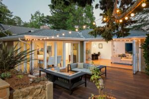 Modern home with a spacious wooden deck, outdoor furniture, and string lights,