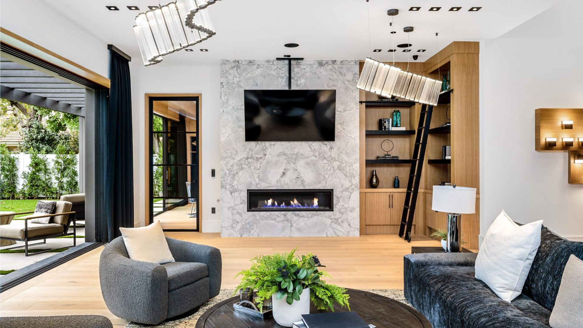 Modern living room interior with stylish furniture, open sliding doors to garden, and a marble fireplace with a TV above.